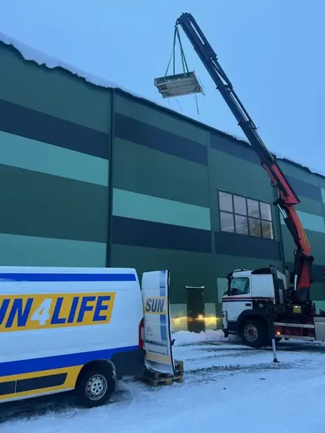 Sun4Lifes servicebil vid en industrihall medan en lastbilskran lyfter upp material på taket.