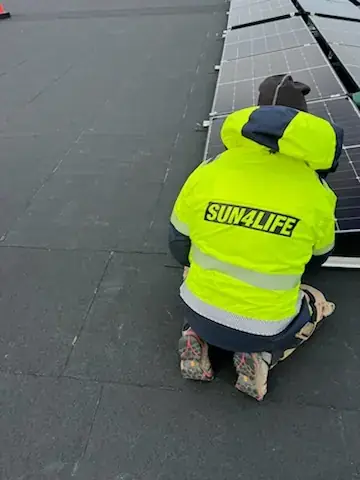 Montör i Sun4Lifes gula varselväst som arbetar med panelrader på ett tak.