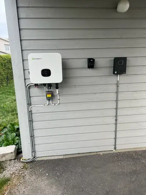 Växelriktare och mätarskåp monterade på en garagevägg.