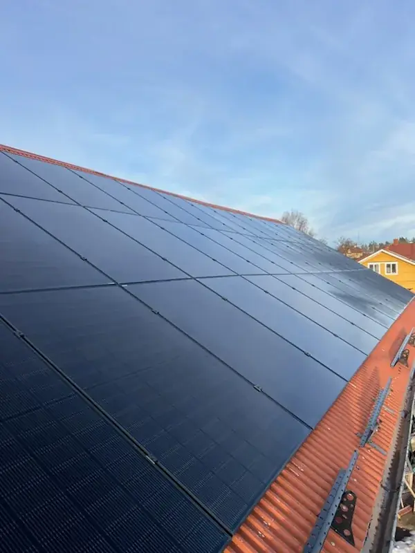 Svarta solpaneler monterade i rader på ett rött tegeltak.