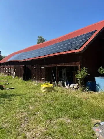 Röd ladugård med solpaneler monterade på det röda tegeltaket, omgiven av gräs.