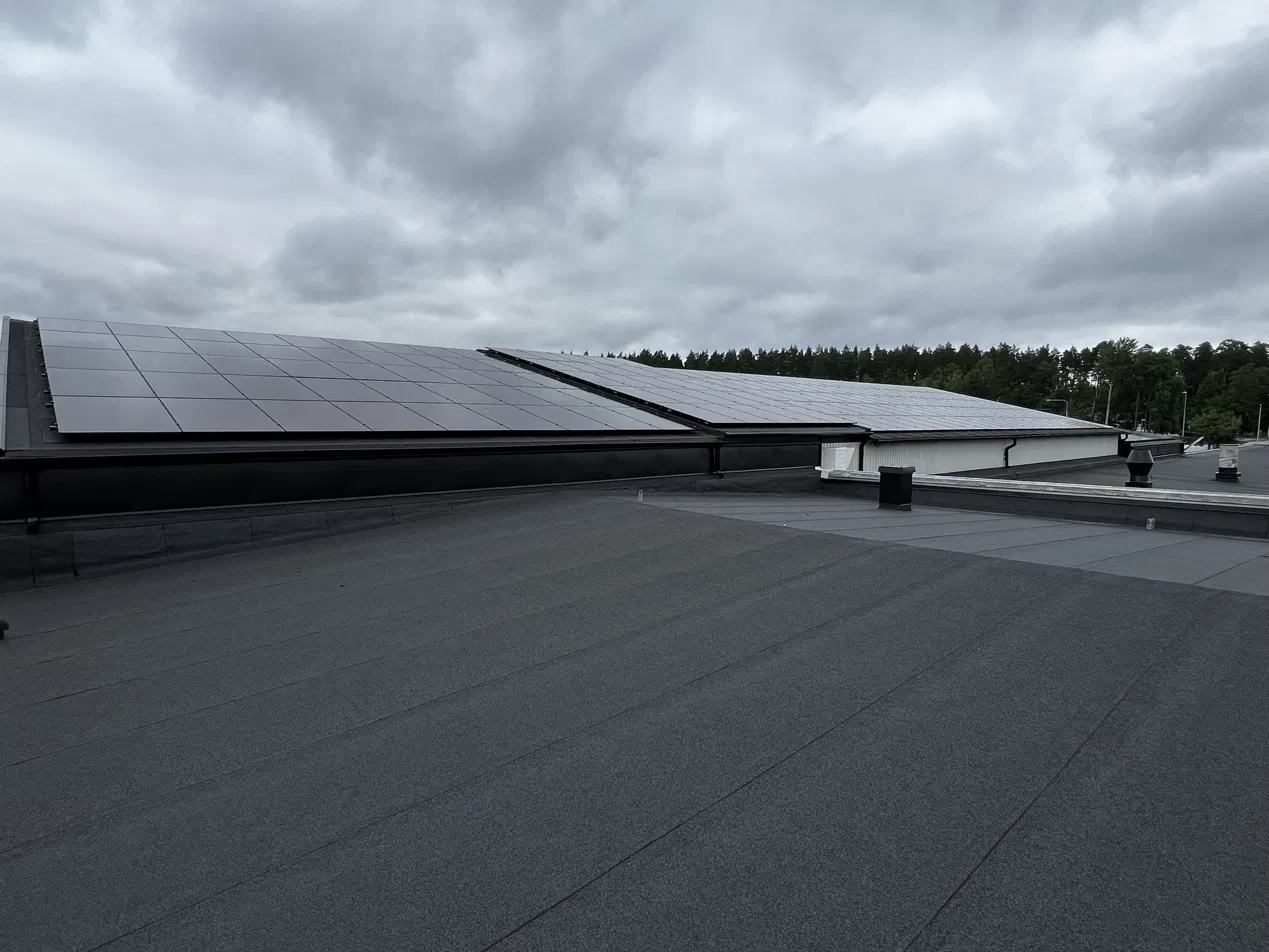 Långa rader av solpaneler på ett industritak under mulen himmel.