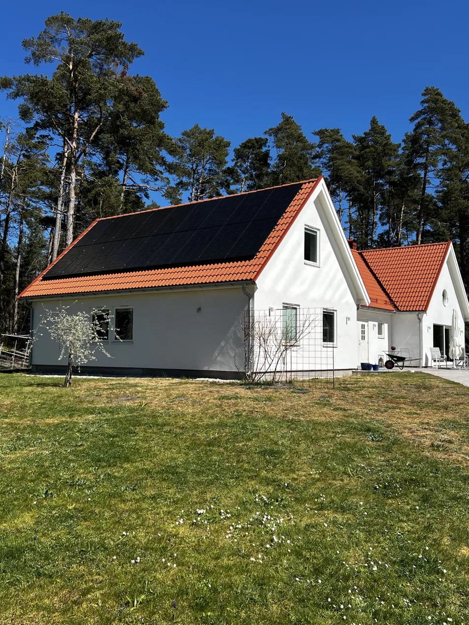 Vitt hus med rött tegeltak och svarta solpaneler en solig dag.