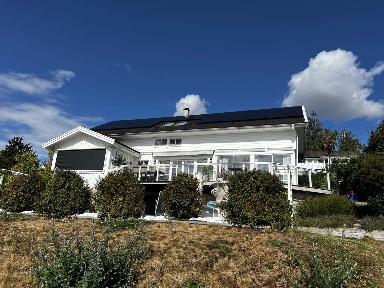 Vit villa med solpaneler på taket, sedd från trädgården en solig dag.