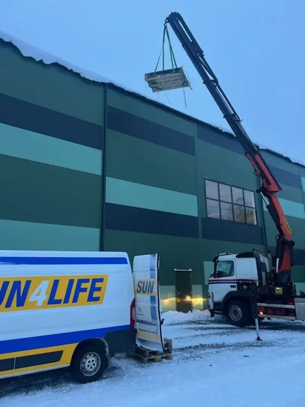 Sun4Lifes servicebil vid en industrihall medan en lastbilskran lyfter upp material på taket.