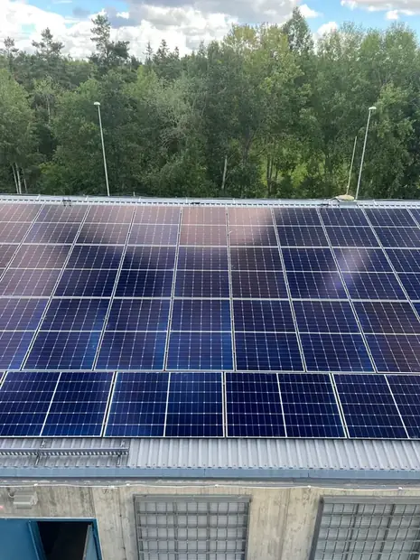 Solpaneler monterade i täta rader på ett plåttak över en industribyggnad.