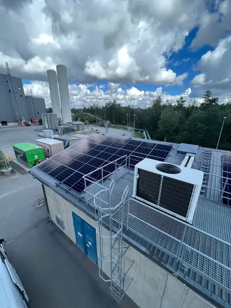 Solpaneler monterade runt ventilationsaggregat på ett platt tak.